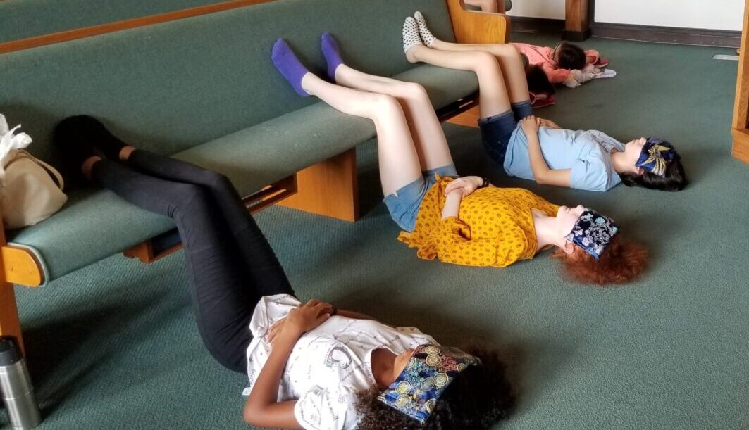 Howard County Flute-a-rama flute camp students relax with legs up on church pew and eye pillows over eyes during yoga for musicians class