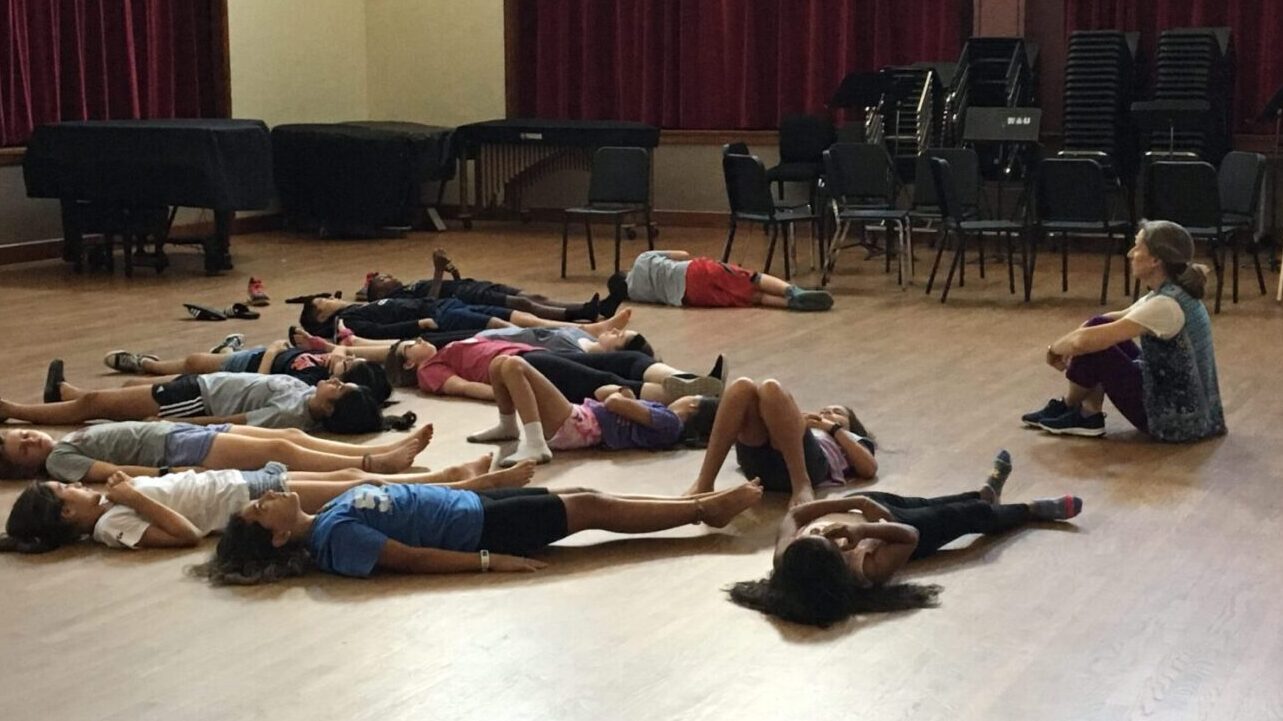 Takoma Park Flute-a-rama flute camp students rest on the floor as teacher Melissa Lindon guides yoga Nidra relaxation practice